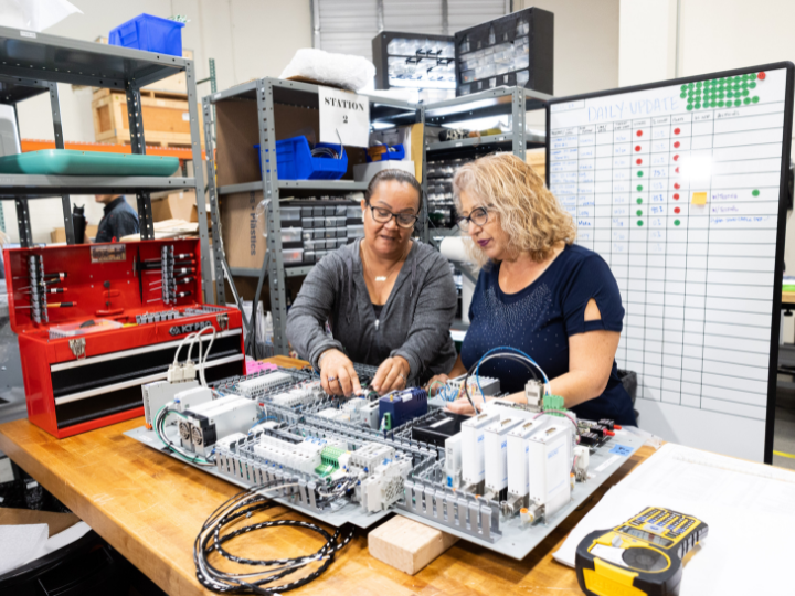 Two women collaborating in a workspace with electronic components, showcasing teamwork and innovation in technology development