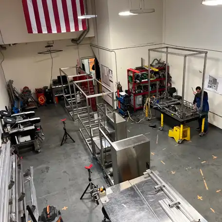 AES Fabrication Workshop in Oceanside, CA, USA, showing a spacious and adaptable workspace with large-scale biotech equipment under fabrication. The workshop features various tools, workstations, and an American flag hanging on the wall.